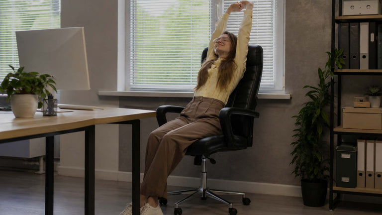 A woman stretching in a black office chair at her desk in a modern home office setting.